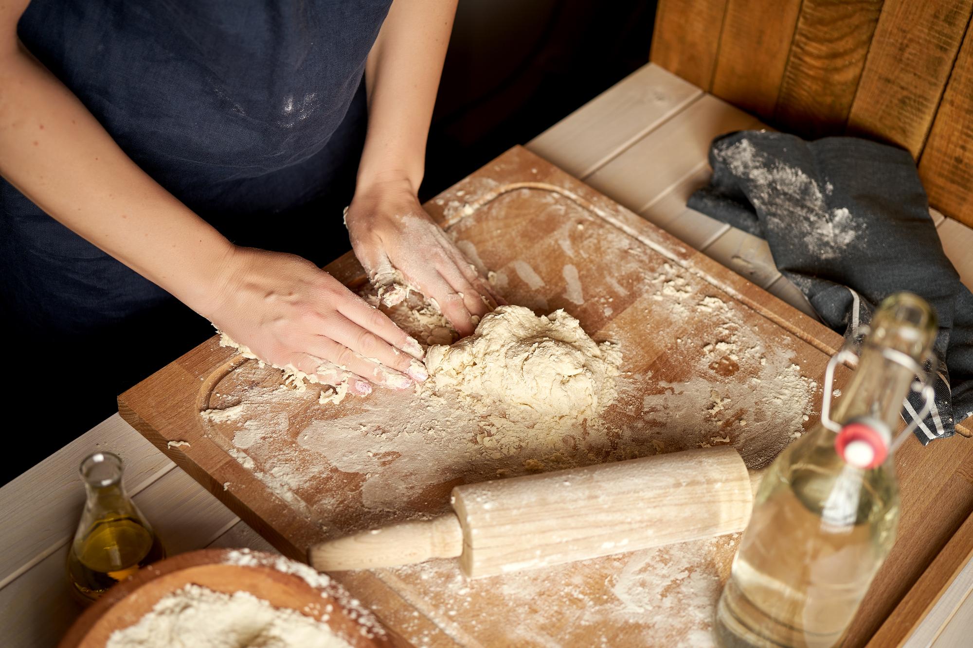 close-up of hands kneading dough on floured board